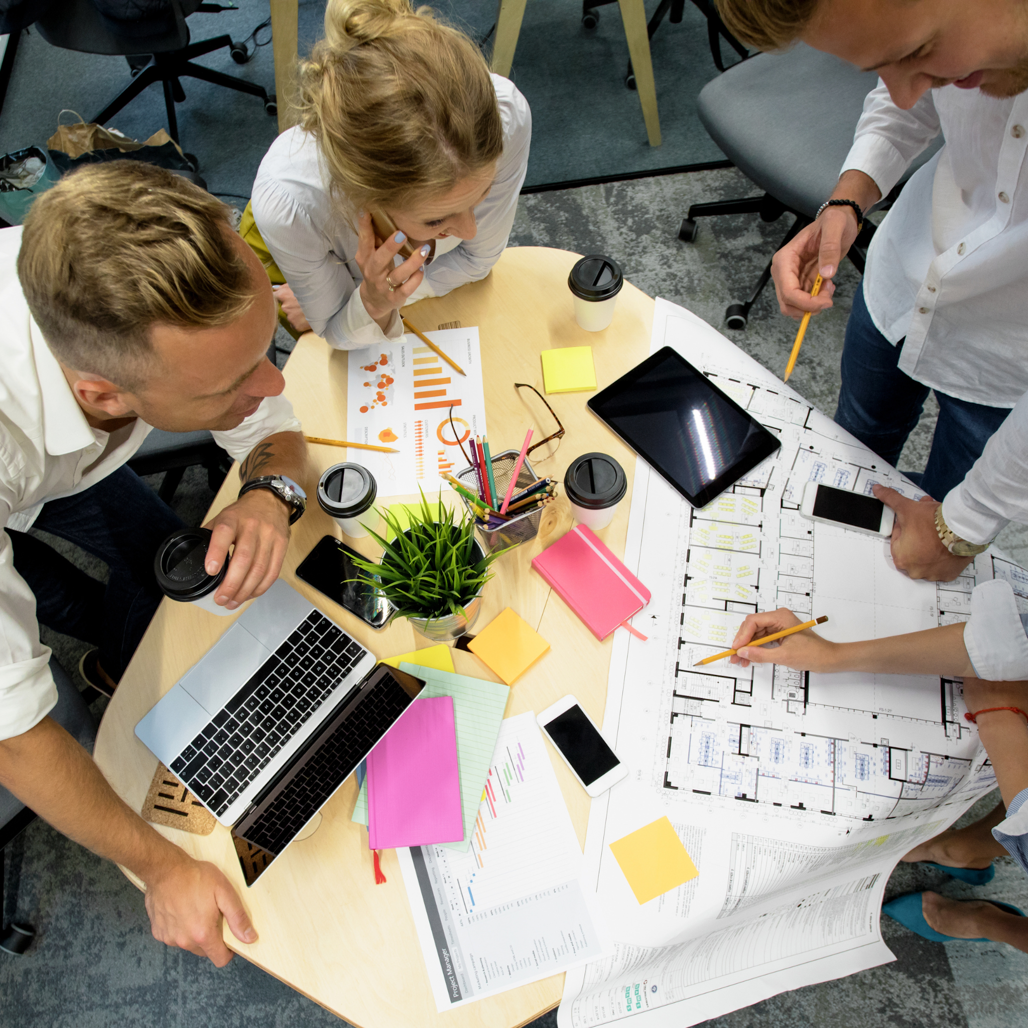 Group of people working together at a table with plans and a laptop