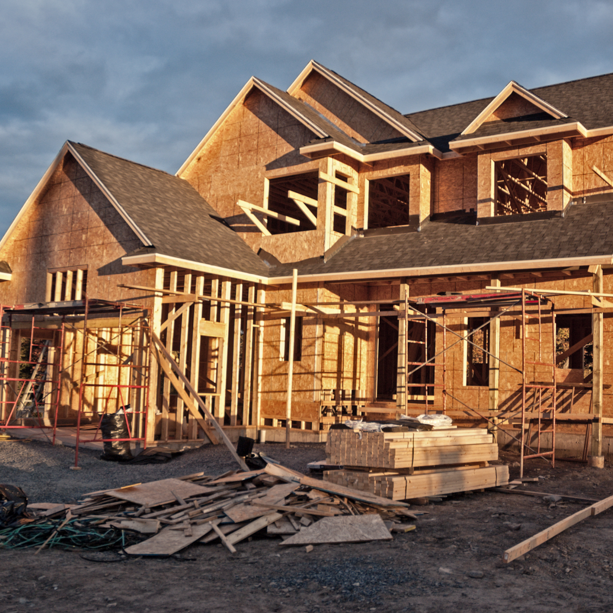 House under construction with wooden framing and scaffolding against a blue sky