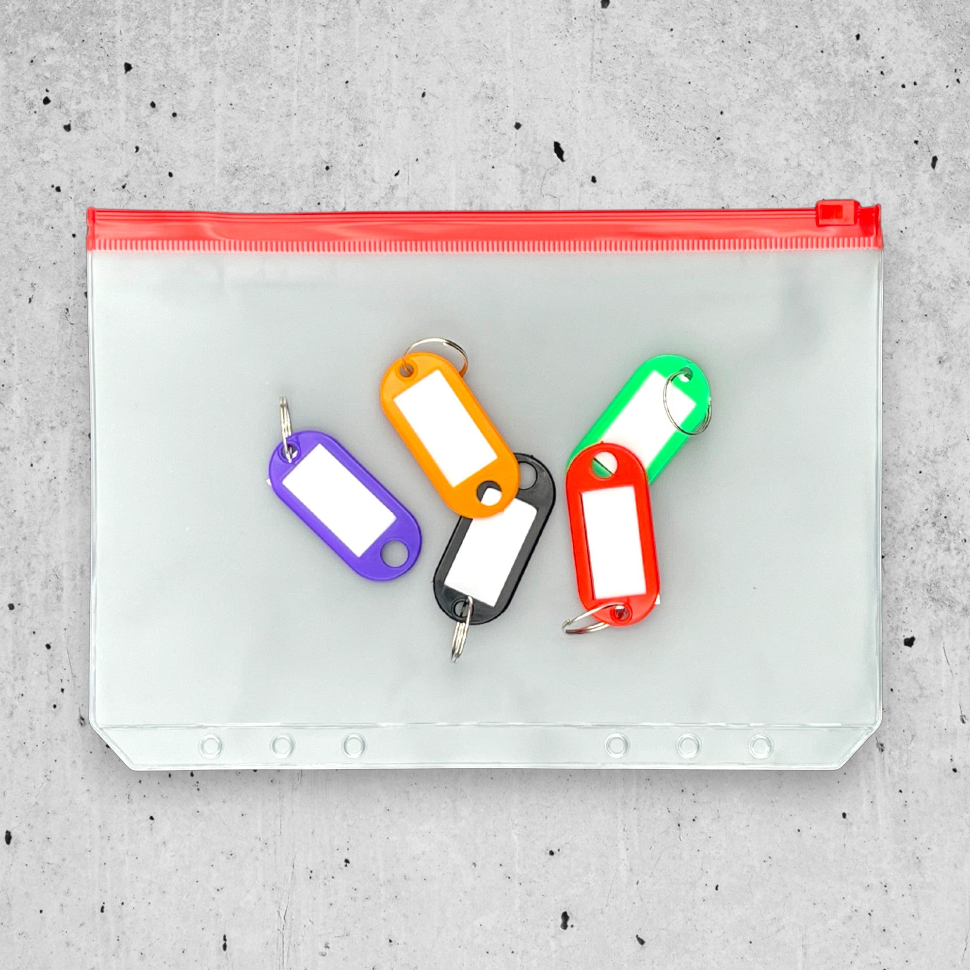 Colorful key tags on a clear pouch with red zipper on a gray concrete surface