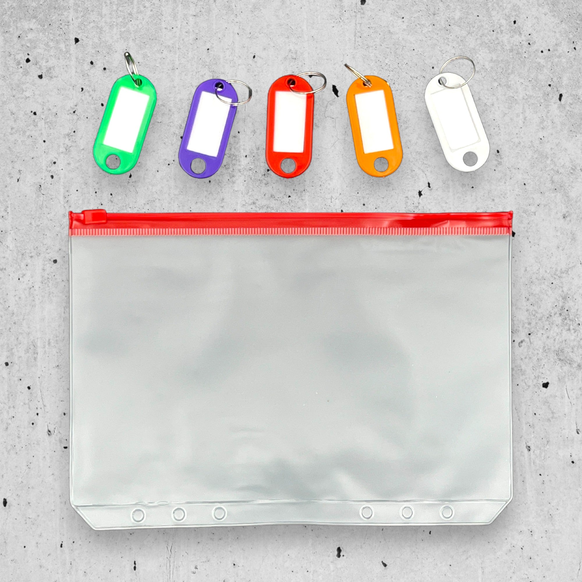 Clear pouch with red zipper and colorful key tags on a gray concrete surface