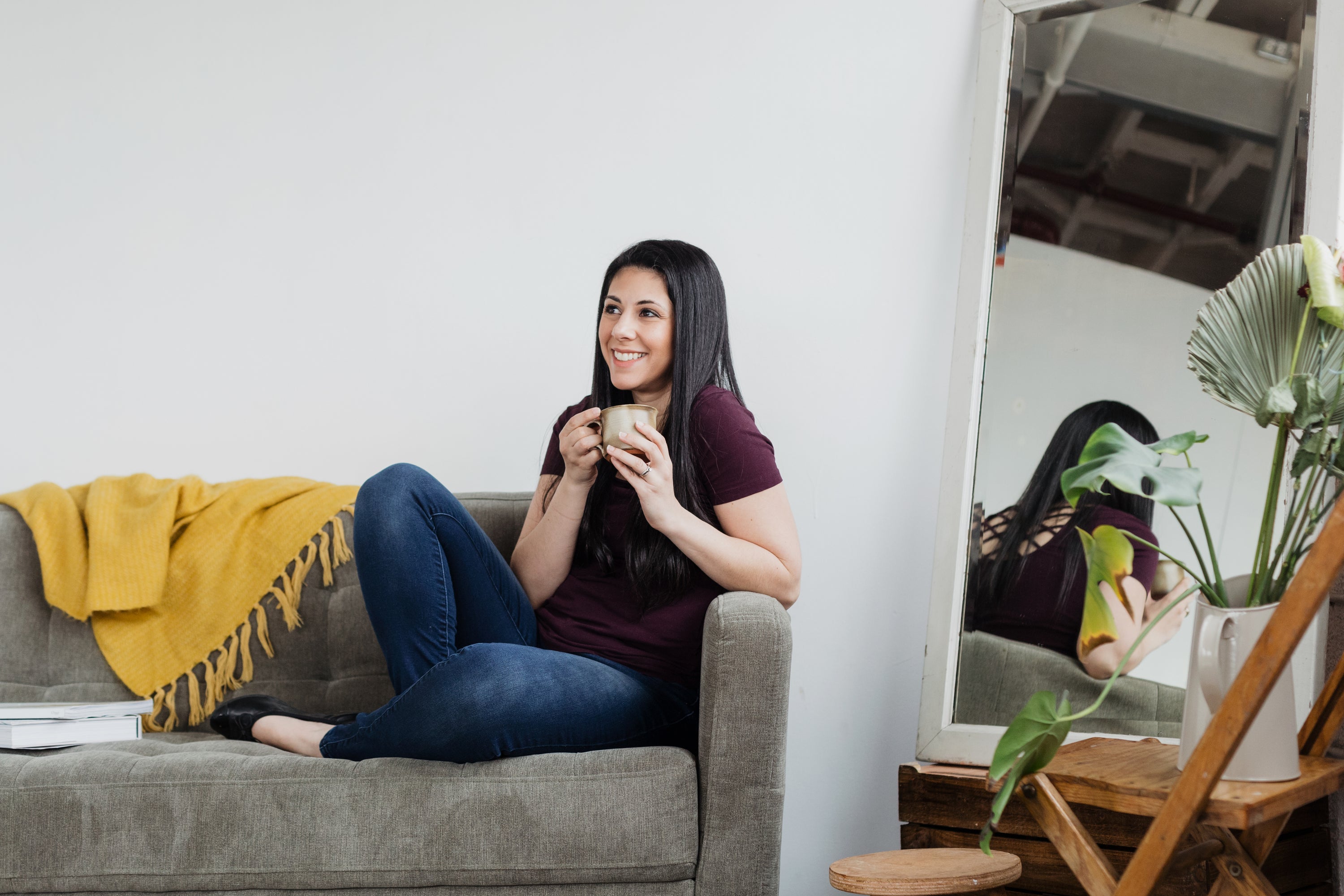 A woman sits on a sofa cradling a cup of coffee in her hands